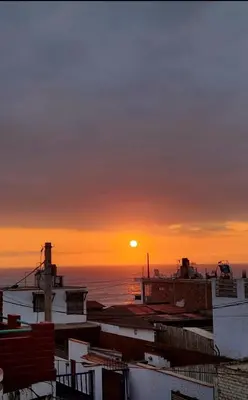 a sunset over the ocean with the roofs of buildings at 
