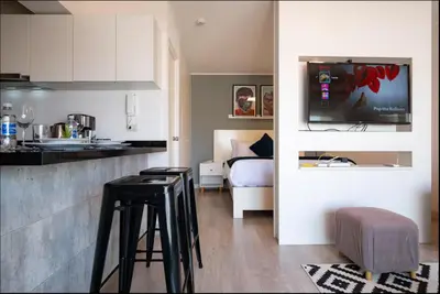 a kitchen with two bar stools and a room with a bed at Stelar Apartments by Vibrant in Lima