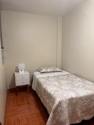 a white bedroom with a bed and a night stand at Light department in Lima
