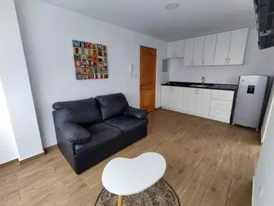 a living room with a black couch and a white stool at Departamento de playa in Lima
