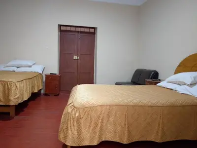 a room with two beds and a chair and a door at Frente al Qorikancha - 2 cuadras Plaza Central in Cusco