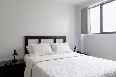 a white bedroom with a bed with white sheets and a window at San Miguel Awanka Hotel in Lima