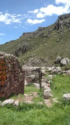 a stone wall next to a grassy hill at Casa Qantu Huaytará in Huaytará