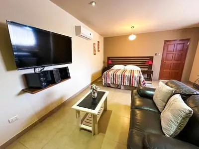 a living room with a couch and a television on a wall at Apart-Hotel El Cañaveral in Chincha