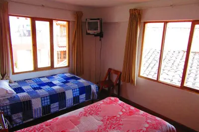 a bedroom with two beds and a tv and windows at Hospedaje Kamila in Cusco