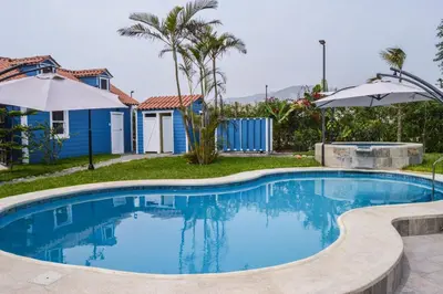a swimming pool with an umbrella and a house at Villa Aurora in Aucallama