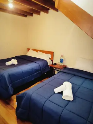 a room with two beds with blue covers and a table at Casa Centro Historico Cusco in Cusco
