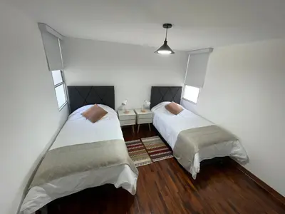 two beds in a room with white walls and wood floors at Dpto Benavides la paz miraflores in Lima