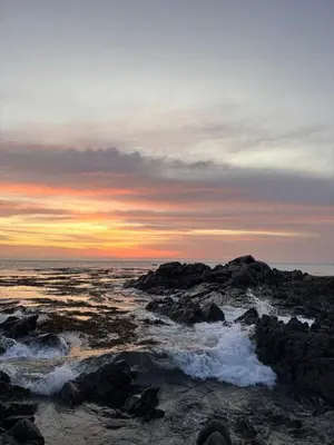 a sunset over the ocean with rocks and water at Tanaka Beach House in Tanaca