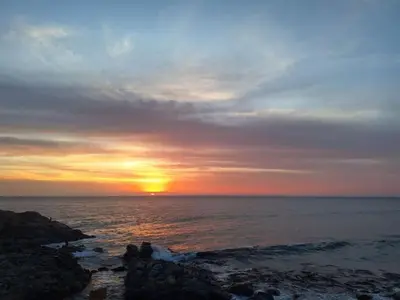 a sunset over the ocean with people on the rocks at Tanaka Beach House in Tanaca
