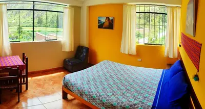 a bedroom with a bed and a chair and windows at Mountainview House Ollantaytambo in Ollantaytambo