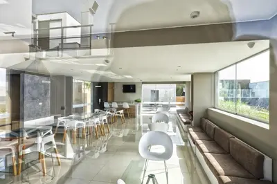 a dining room with white chairs and tables and windows at Wasi Apartment Pardo in Lima