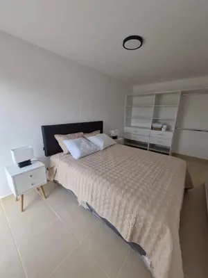 a white bedroom with a bed and a night stand at Departamento a un paso de playa Pulpos y Arica in Lurín