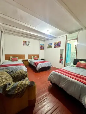 a room with three beds and a chair in it at Posada Escondida in Cusco