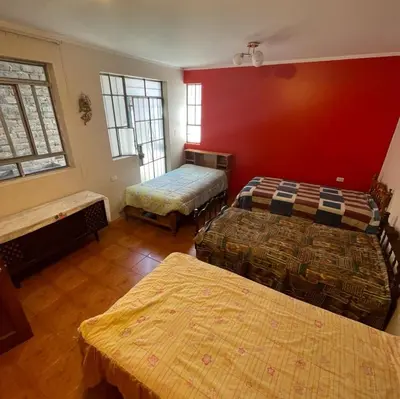 a room with two beds and a red wall at Habitación para 4 personas a pasos de la plaza de armas in Ayacucho