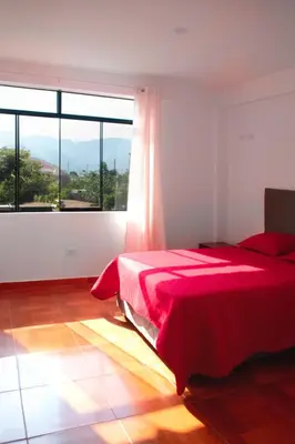 a bedroom with a red bed and a large window at Kampu Wasi - Casa de Campo in Pachacamac