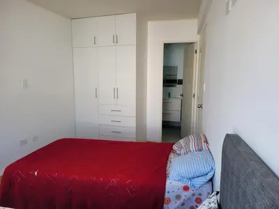 a bedroom with a bed with a red blanket and a chair at 1cuarto 2 camas baño privado in Lima