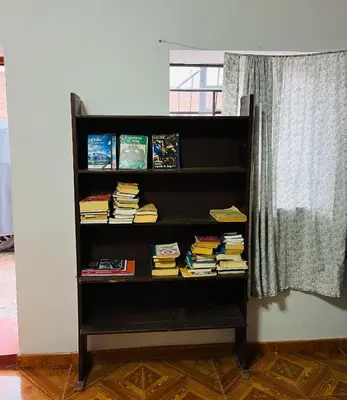 a book shelf filled with books next to a window at hostel arcoiris urubamba in Urubamba