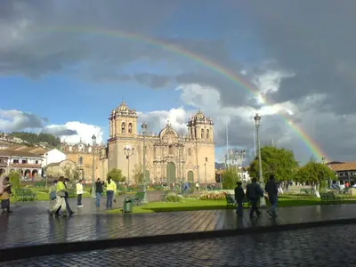 a group of people walking in front of a cathedral with a rainbow at Hostal Lucerito in Cusco