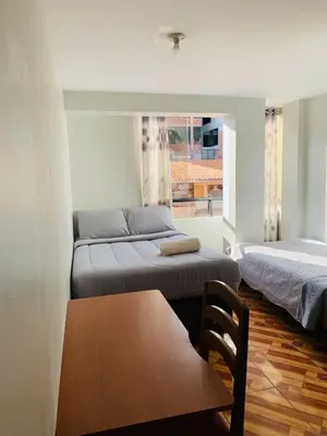 a room with two beds and a table and a window at Hostal El Mariscal in Urubamba