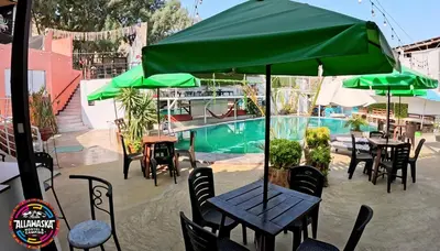 a patio with tables and green umbrellas next to a pool at Allawaska Hostel & Camping in Laguna Huacachina