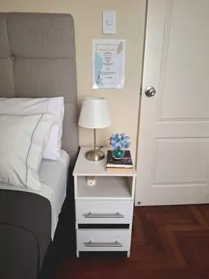 a bed with a white nightstand with a lamp and a book at Room in shared apartment - Shared Bathroom 402 in Lima