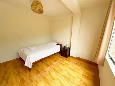 a bedroom with a white bed and a wooden floor at Departamento Maranura Quillabamba in Maranura