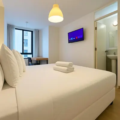a bedroom with a large white bed with a tv on the wall at Suite Ocean View con WiFi San Miguel 1502 in Lima