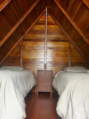 a attic bedroom with two beds and a wooden wall at ALPHINA CABINS Qhapaq Ñan in Sahuayacu