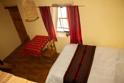a bedroom with a bed and a chair and a window at Hospedaje Pumayalli in Urubamba