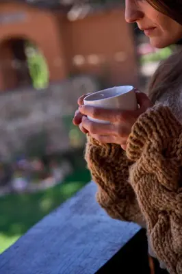 a woman holding a coffee cup in her hands at Piedra Wasi Ecolodge Urubamba in Urubamba