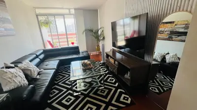 a living room with a black leather couch and a mirror at A 15 minutos del aeropuerto cómodo y moderno departamento de 3 habitaciones independientes y 2 baños in Lima