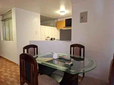 a glass table in a room with chairs and a kitchen at Cusco Hermoso in Cusco