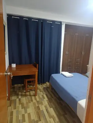 a bedroom with a bed and a desk with a blue curtain at Departamento Frente al Cc Mega plaza - Ica in Ica