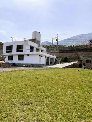 a white building with a field in front of it at Viña J Felix in Lunahuaná