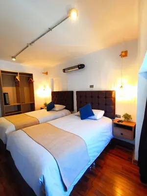 two beds in a hotel room with white sheets and blue pillows at Apartamento Céntrico in Cusco