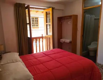 a bedroom with a red bed and a door to a bathroom at Tambo de Ollantay Hotel in Ollantaytambo