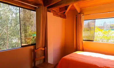 a bedroom with a bed and two large windows at Tambo de Ollantay Hotel in Ollantaytambo