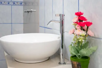 a bathroom with a sink and a vase with red flowers at Inkary Hotel Machupicchu in Machu Picchu