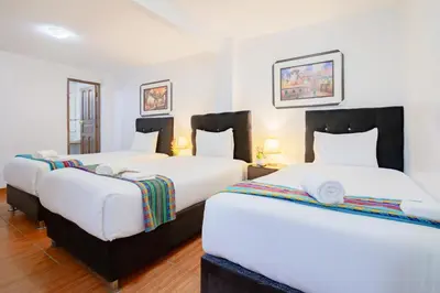 two beds in a room with white walls and wood floors at Inkary Hotel Machupicchu in Machu Picchu