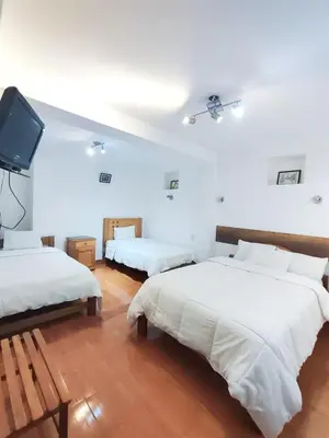 a white room with two beds and a tv at Hoteles Romero in Machu Picchu