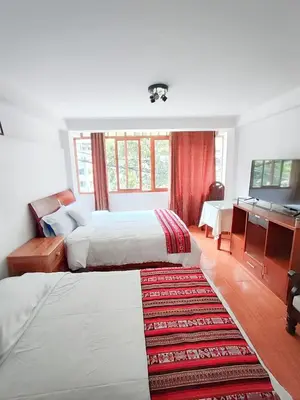 a bedroom with two beds and a desk and a television at Hoteles Romero in Machu Picchu