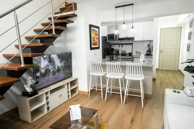 a living room with a staircase and a kitchen with white stools at Mezanine Deluxe Miraflores in Lima