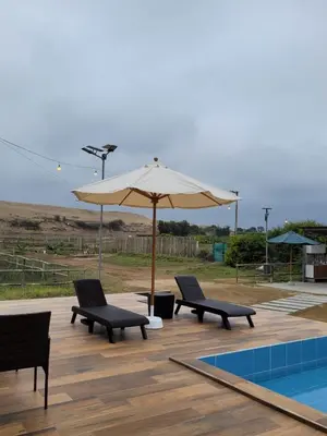 a patio with two chairs and an umbrella next to a pool at Casa de Campo La Martina con piscina y parrilla in Tambo de Mora