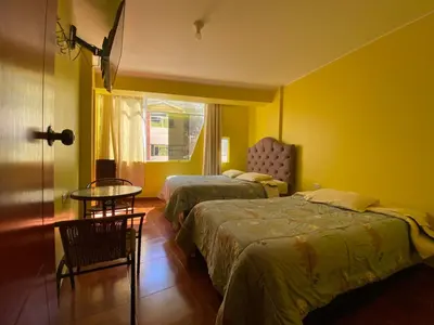 a bedroom with two beds and a table and a window at Churin Hostal J&D in Churín