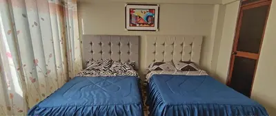 a bedroom with two beds with blue sheets and aintendent at Hostal Casa Blanca in Ayacucho
