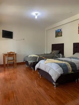 a room with two beds and a table and a television at Habitación triple in Huayllabamba