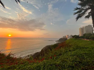 a sunset on the beach with the ocean and buildings at Close to the beach, Big beds, Malecon Miraflores in Lima