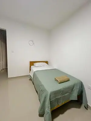 a bed in a white room with a green blanket at La Casita de Condoray - Lunahuana in Lunahuaná