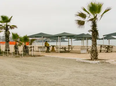 a person standing on a beach with tables and umbrellas at Departamento con salida a la playa Punta Rocas 202 in Punta Negra